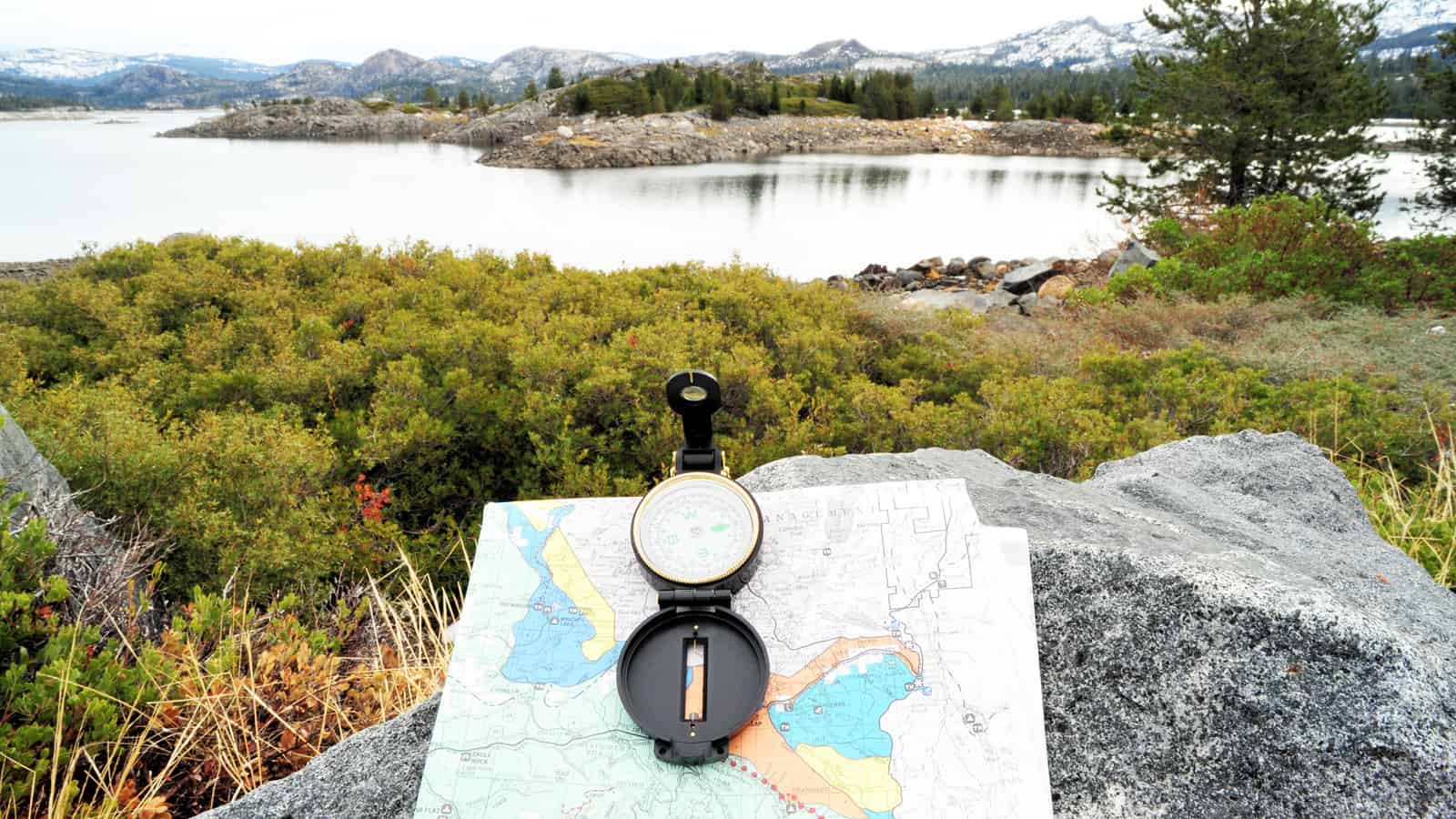 A hiking map and compass overlooking a lake in the California sierra Nevada mountains