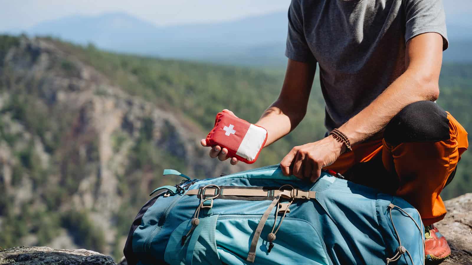 Take a first-aid kit in a backpack on a trip, a hand holds a first aid kit against the background of mountains