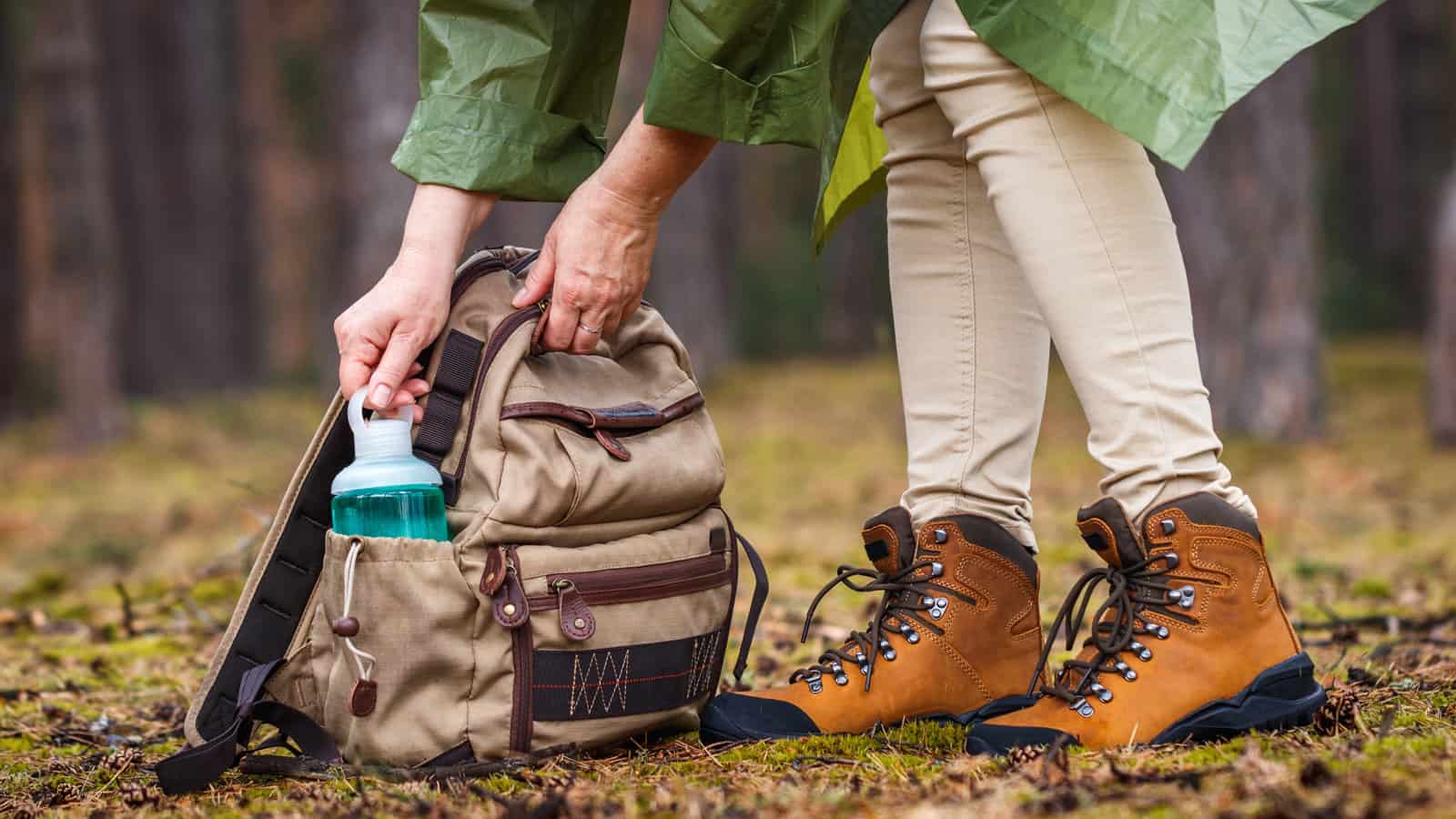 Woman with raincoat and hiking boots taking out water bottle from backpack