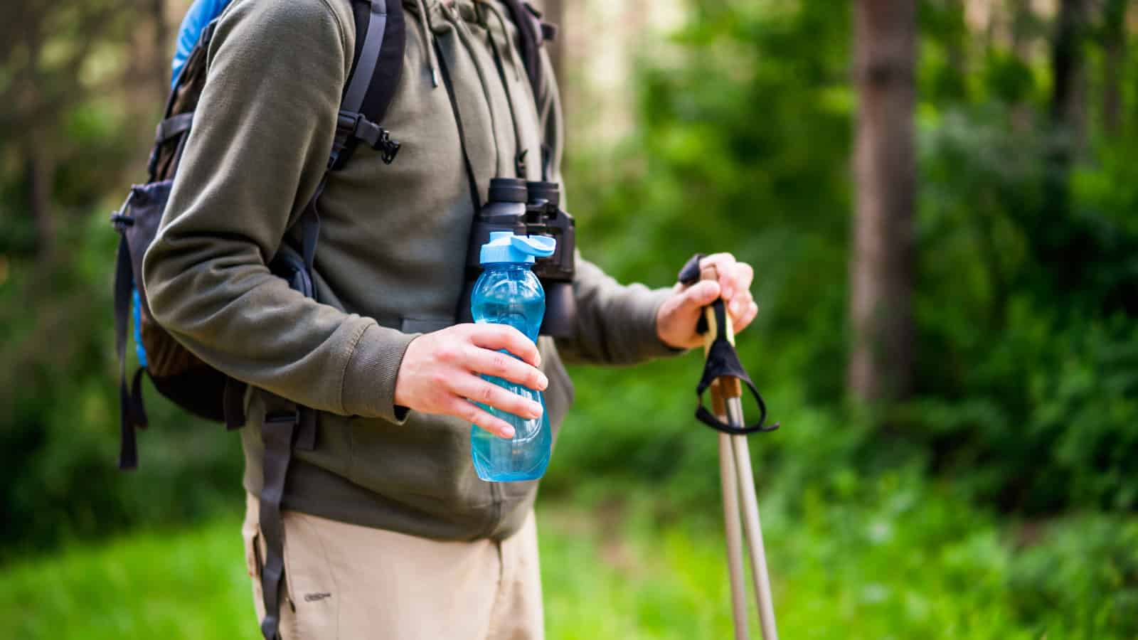 mage of man holding bottle of water and hiking
