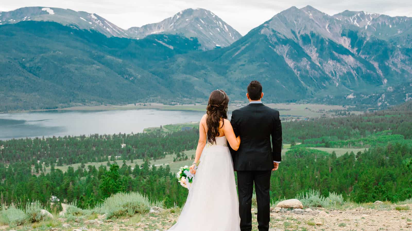 Bride and groom facing toward the rocky mountains and mountain lake. Summer wedding in Rocky Mountain National Park Colorado